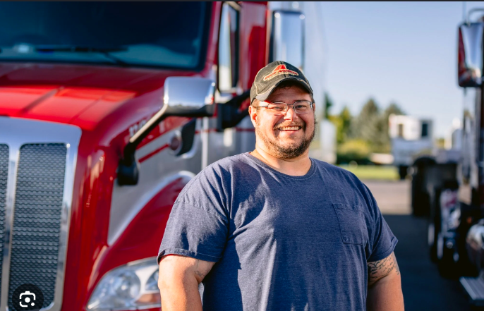 Smiling CDL truck driver standing in front of a red semi truck